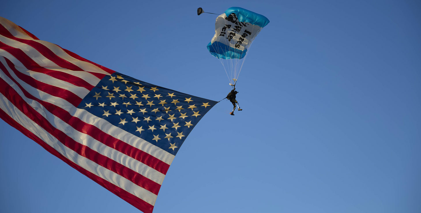 A veteran wearing a parachute is presenting the American flag falling from the sky.